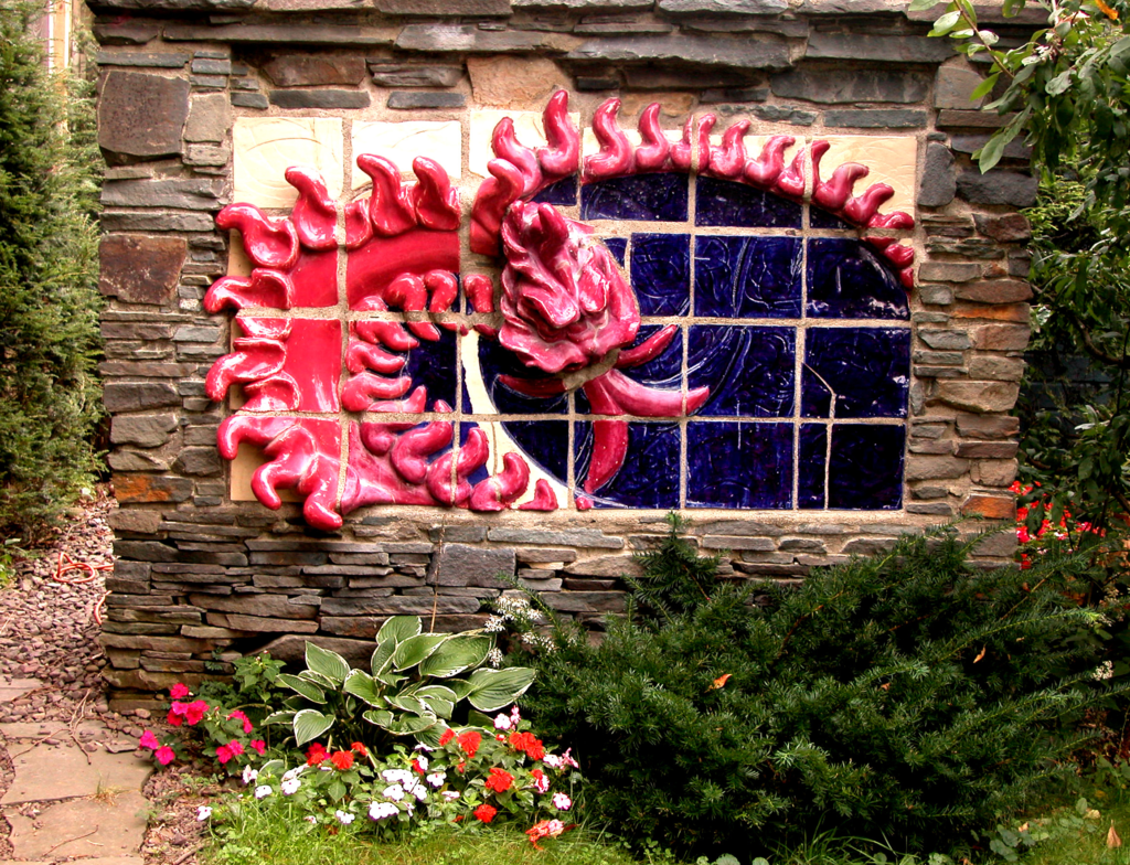 In this monumental 4 x 8 foot stoneware bas relief, the red dragon thrusts outward from a flat plane, its body projecting into three dimensions. Glazed in a deep, resonant red, the Wyrm burns with mythic fire — a guardian forged in clay and flame, cemented into a Catskill Mountain bluestone wall.
