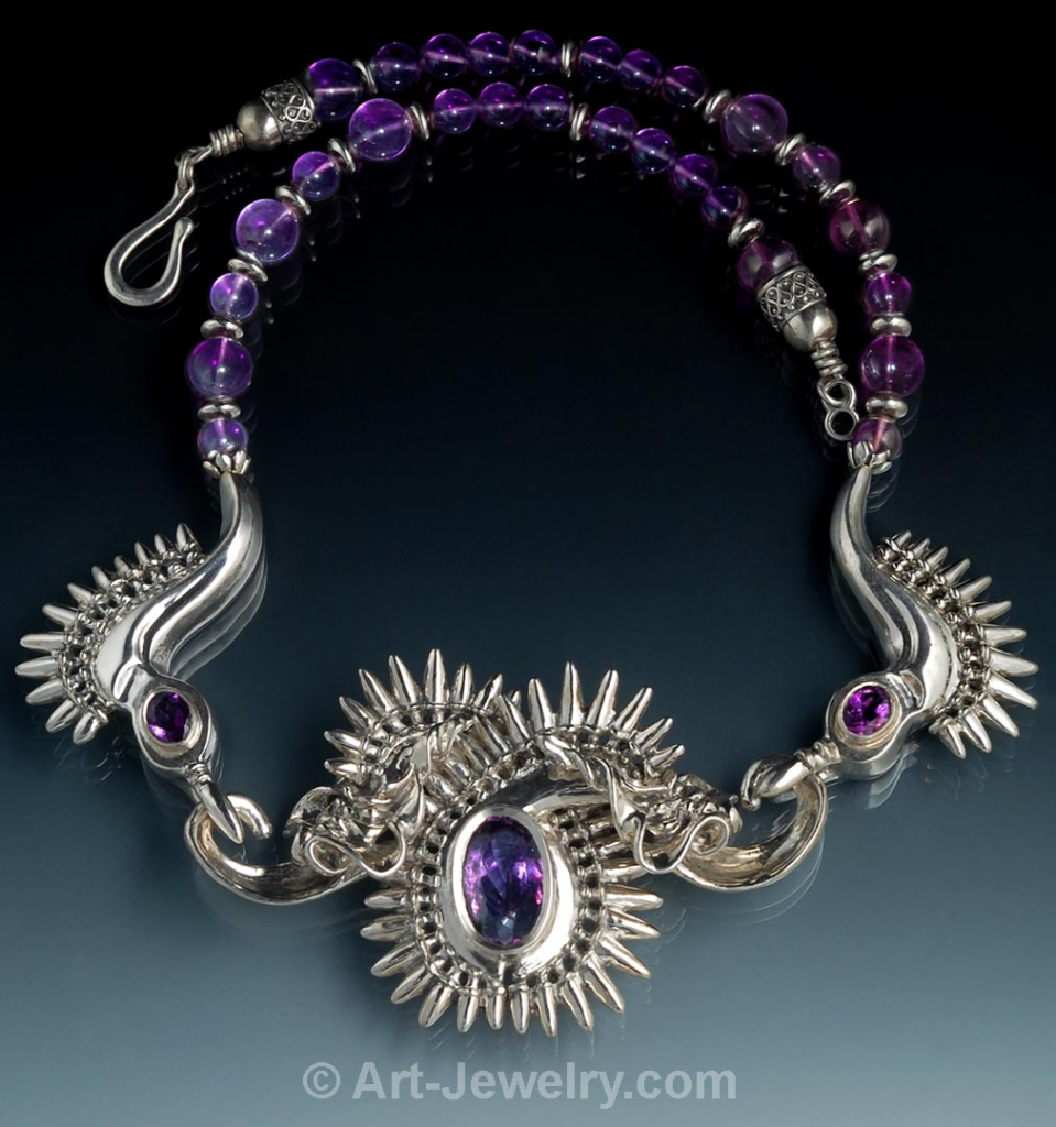 Hand‑carved two‑headed sterling silver dragon necklace with custom hammer‑set amethyst gemstones and sculpted wings.