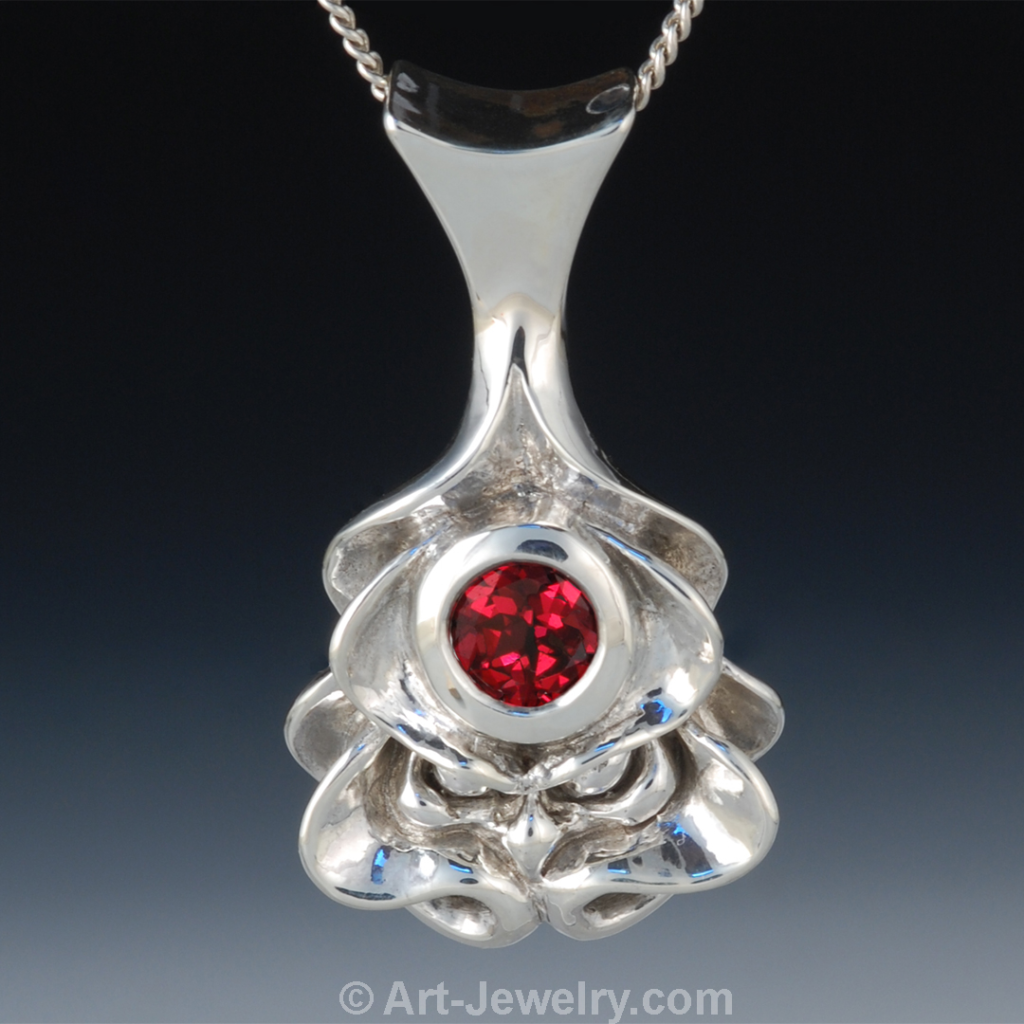 Hand‑carved sterling silver Tatsu dragon face pendant with a hammer‑set garnet spiritual eye and forged bail.